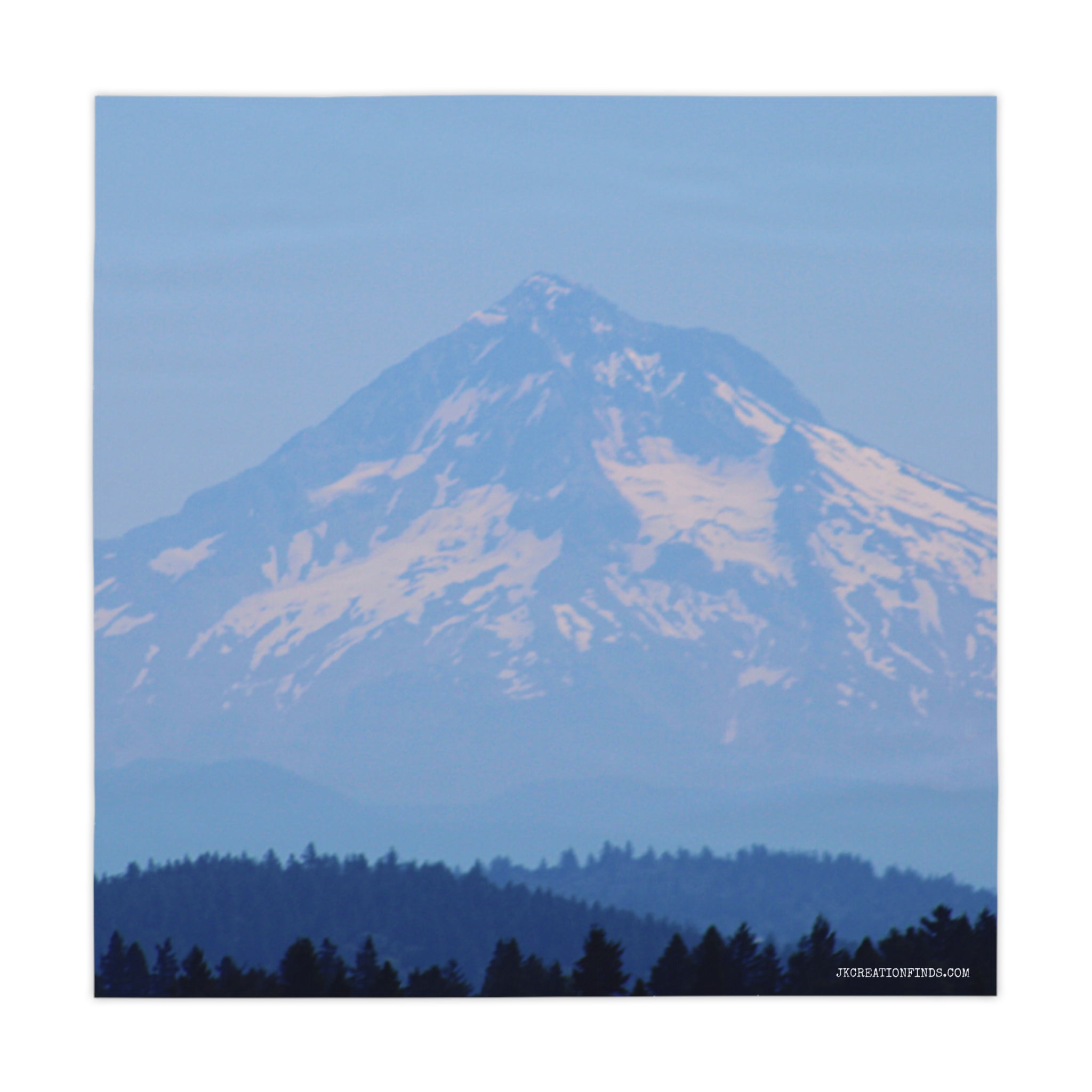 Snow-capped mountain range with blue forest in foreground.