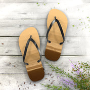 Flip-flops with beach scene straps on white wooden planks with scattered petals.