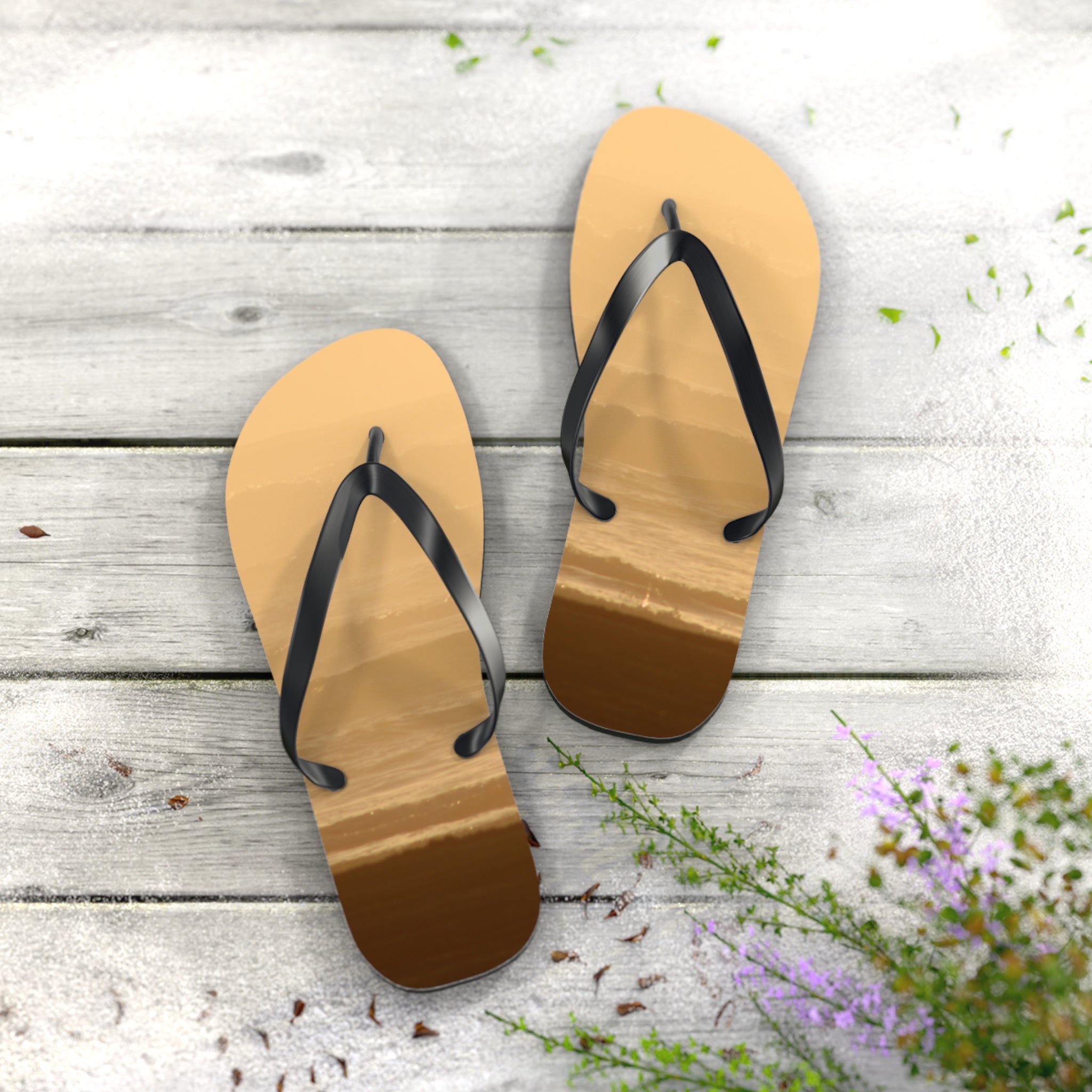 Flip-flops with beach scene straps on white wooden planks with scattered petals.