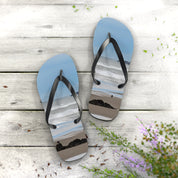 Light blue flip-flops with beach scene graphic on weathered wood background.