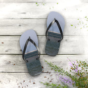Light blue flip-flops with a water scene on the soles, on a wooden deck.