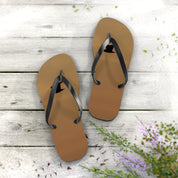 Brown flip-flops with black straps on a wooden background with scattered petals.