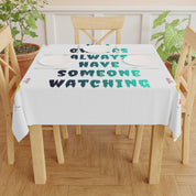 Tablecloth with "Always Have Someone Watching" text on a wooden table.