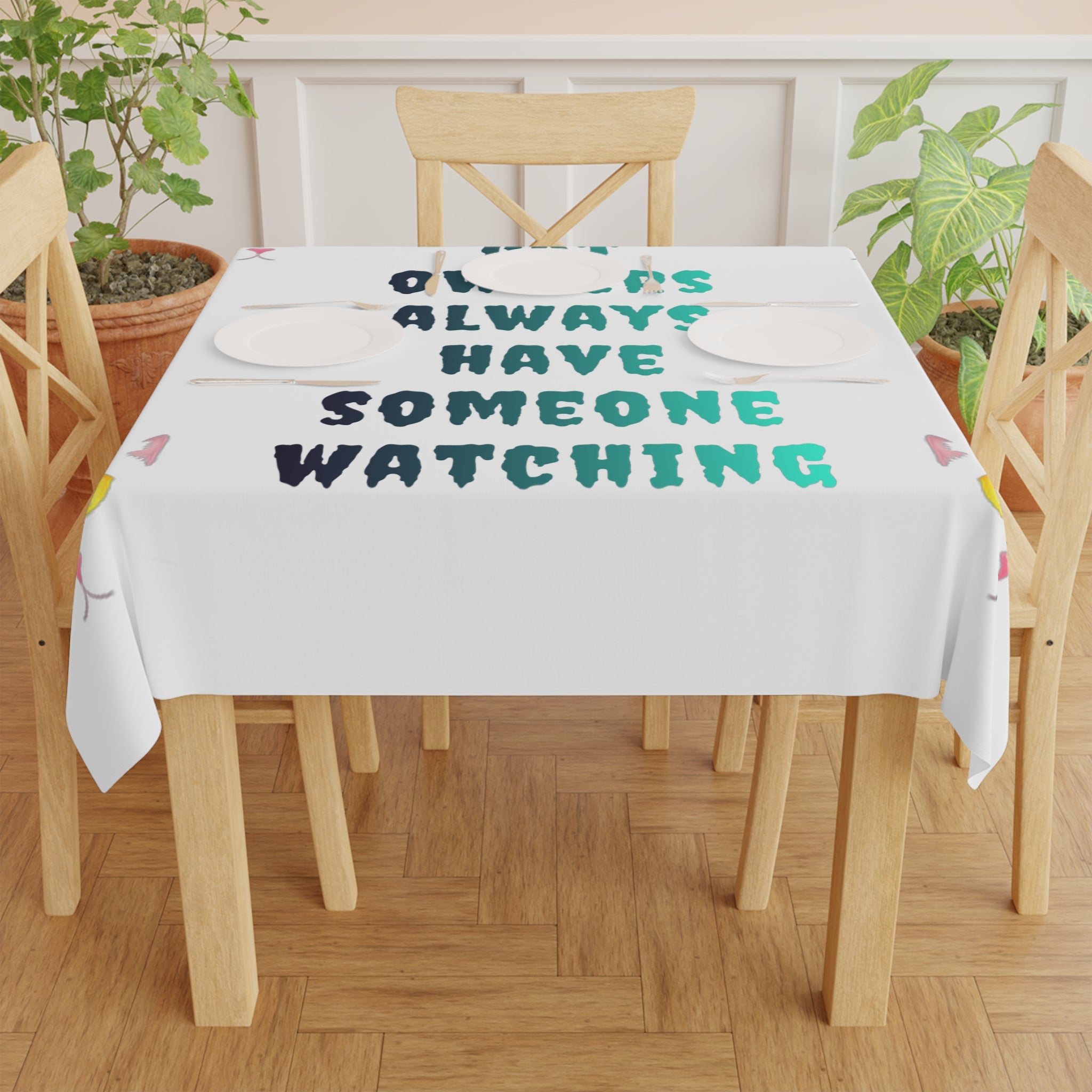 Tablecloth with "Always Have Someone Watching" text on a wooden table.