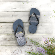 Black flip-flops with waves on the straps, on a white wooden surface.