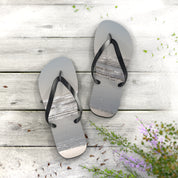 Flip-flops with ocean beach scene on a wooden deck with scattered sand.