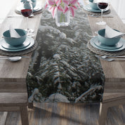 Snowy pine trees on a table runner with pink flowers in vase.