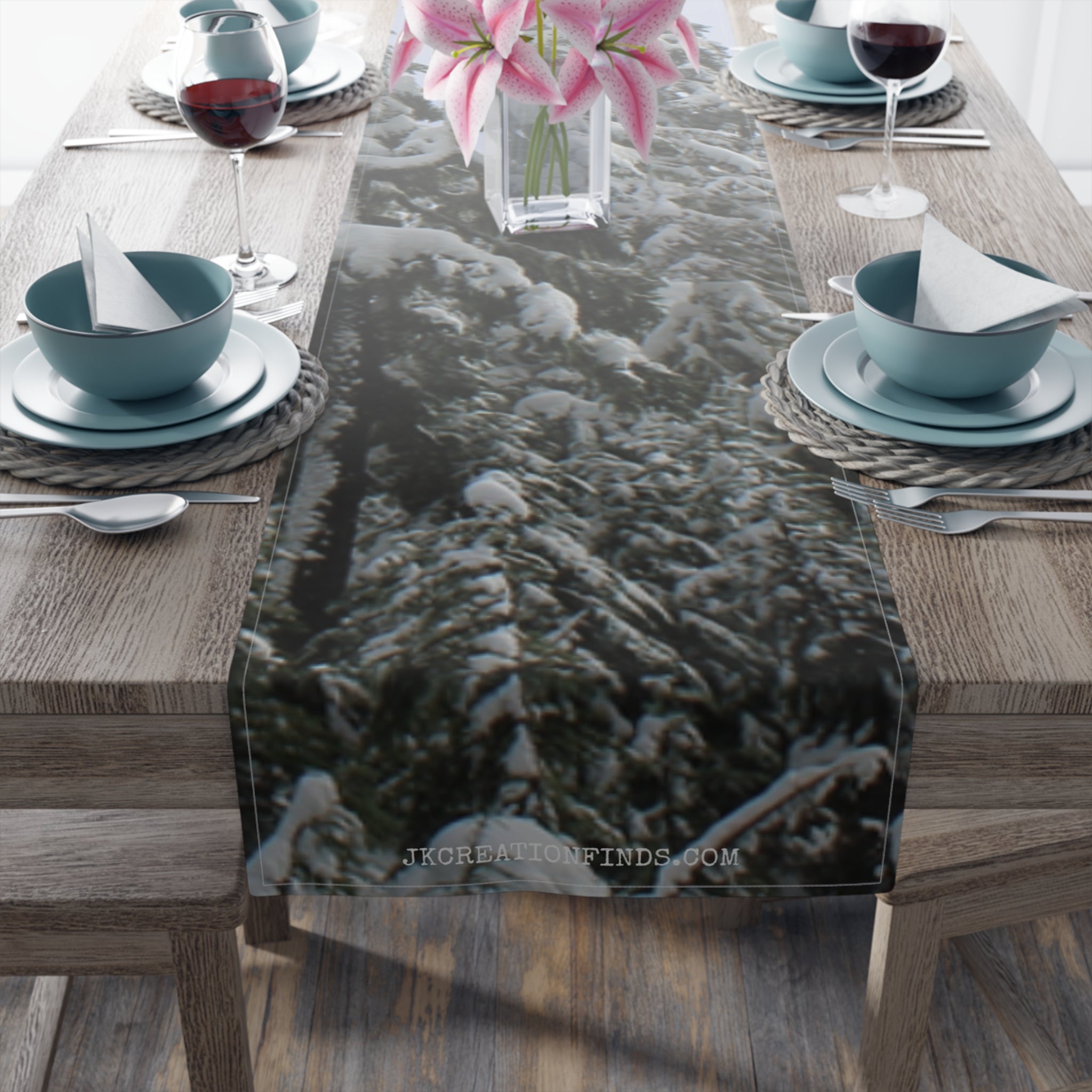 Snowy pine trees on a table runner with pink flowers in vase.