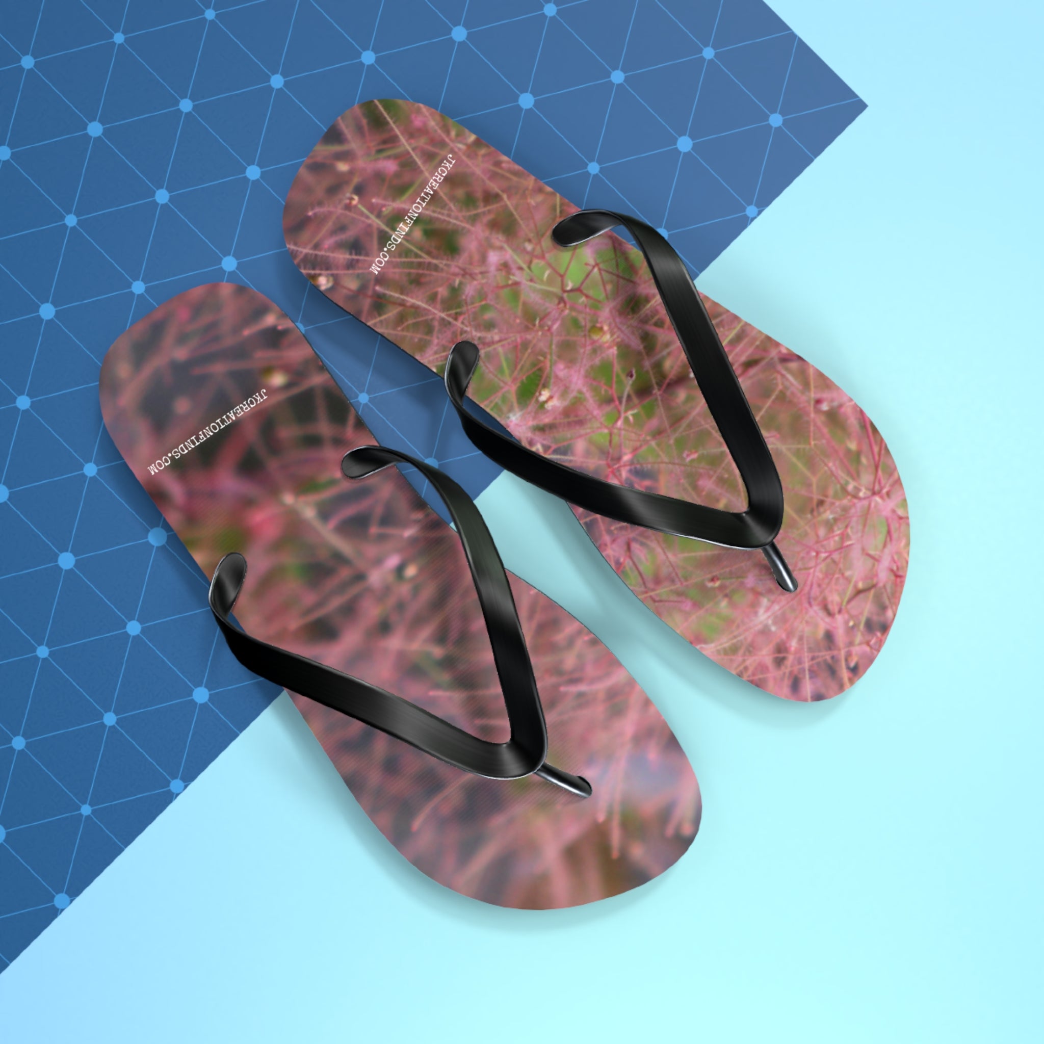 Pink floral flip-flops with black straps on a blue geometric background.