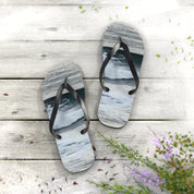 Beach scene flip-flops on a light wooden deck with scattered petals.