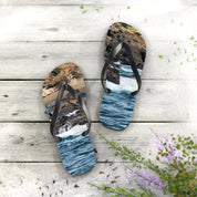 Flip-flops with ocean wave and rocky shore scene on soles, on wood.