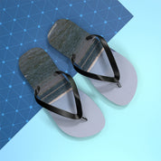 Gray flip-flops with black straps on a blue patterned background.