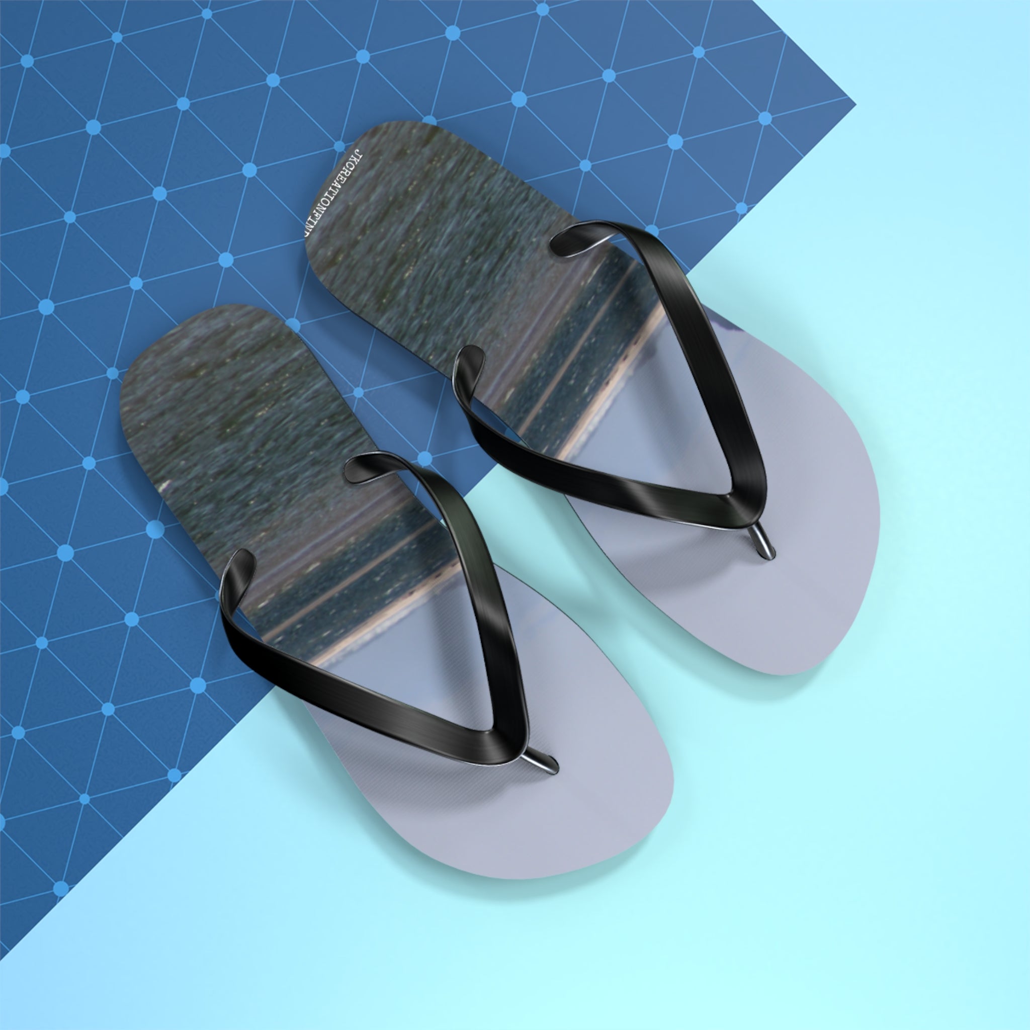 Gray flip-flops with black straps on a blue patterned background.