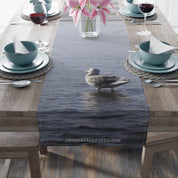 Seagull standing in water with flowers and tableware on a table runner.
