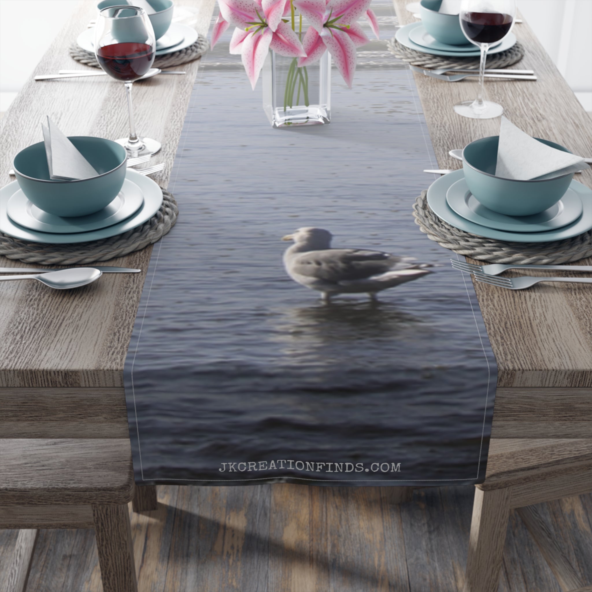 Seagull standing in water with flowers and tableware on a table runner.