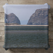 Rocky coastal arch and formations with calm water in the foreground.