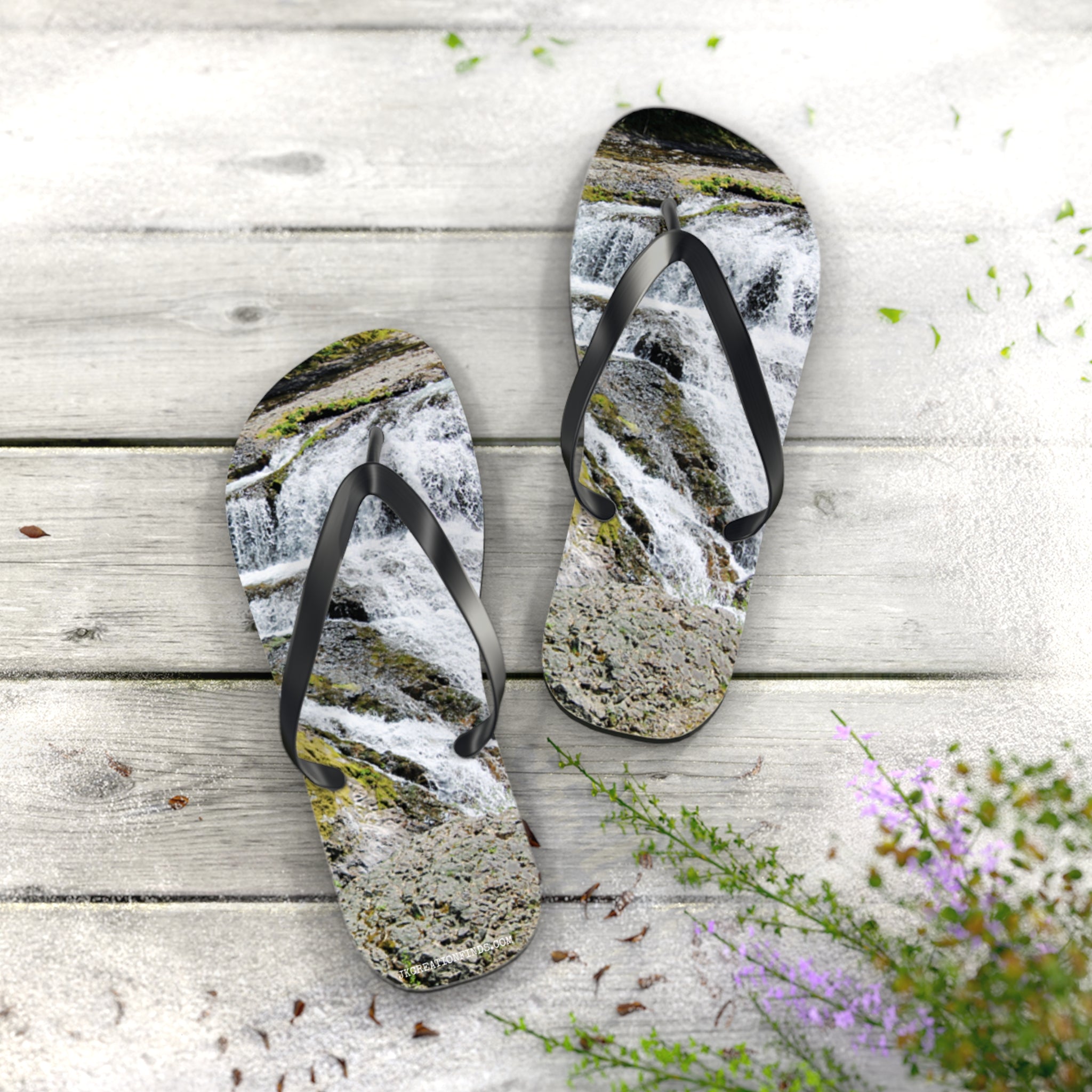 Flip-flops with a waterfall scene on a wooden deck with small plants.
