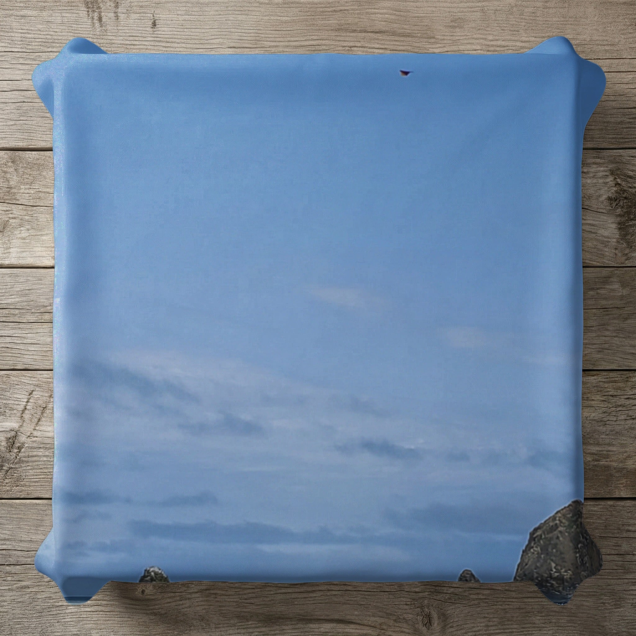 Blue sky with clouds and rocky outcropping above a wooden surface.