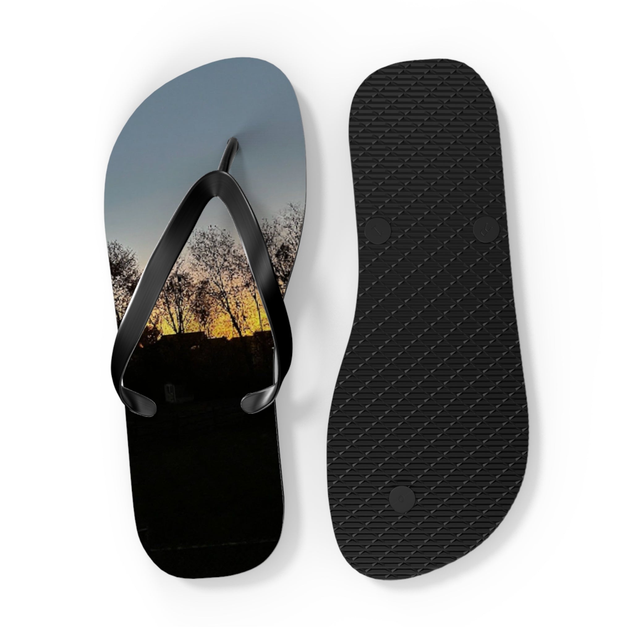 Black flip-flops with a sunset landscape print on the soles.