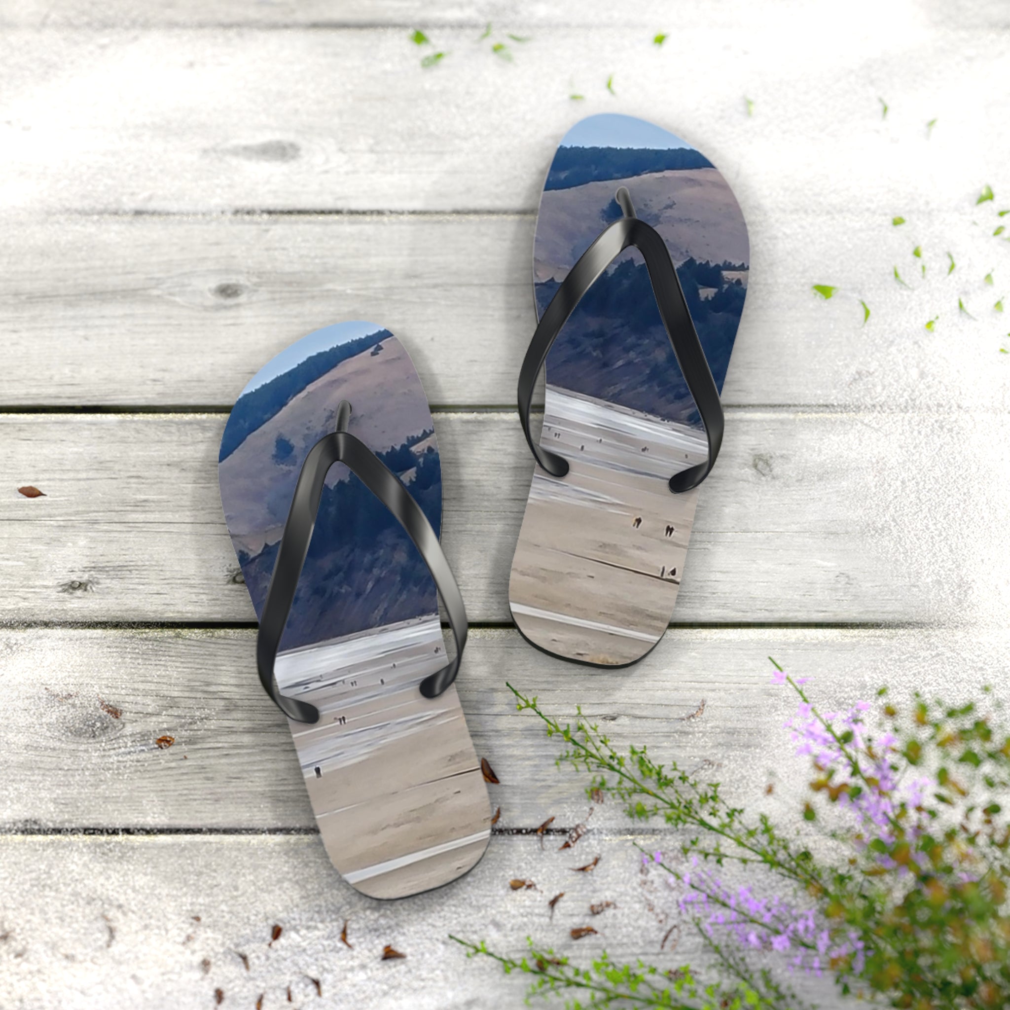 Flip-flops with a beach scene printed on the soles, resting on a wooden deck.