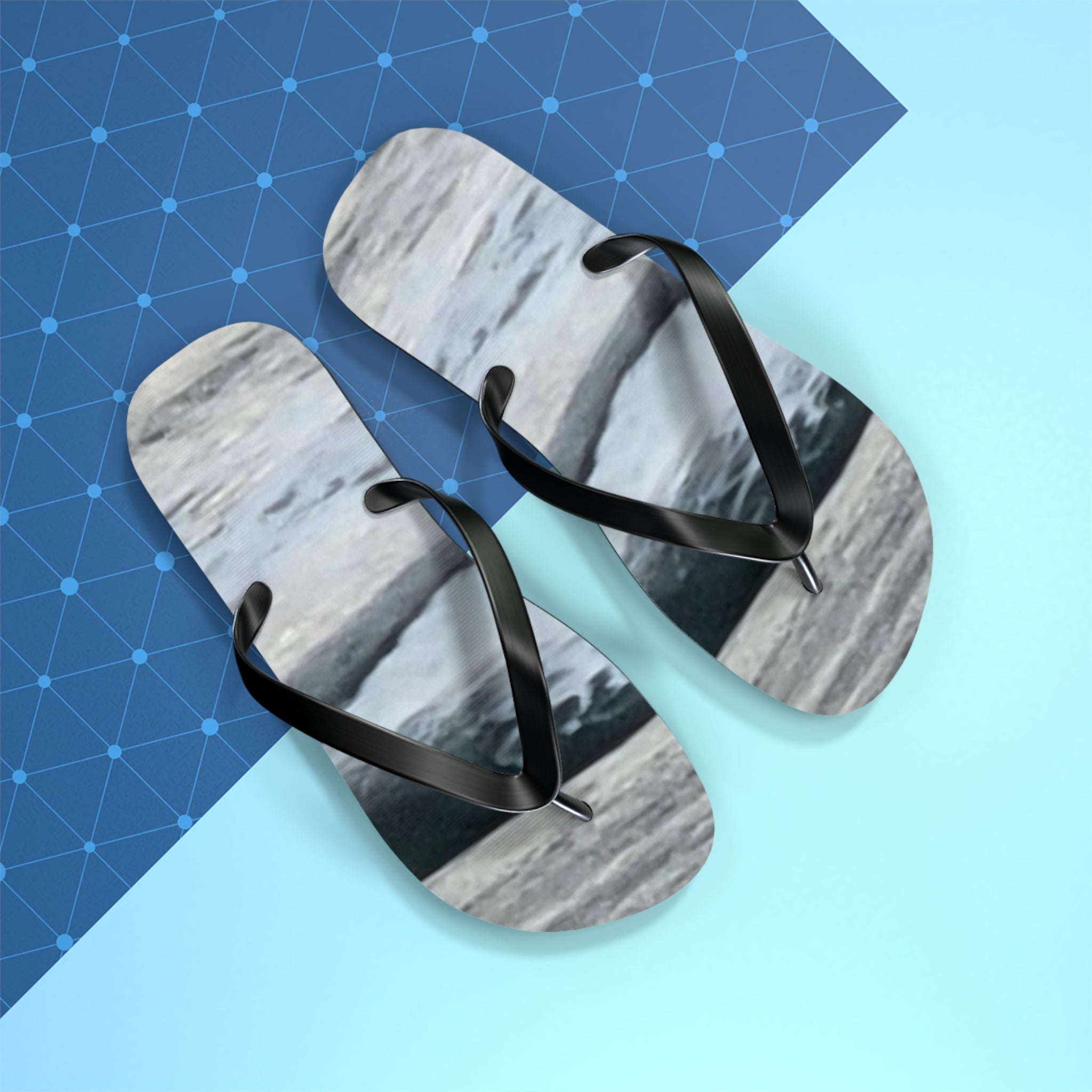 Black flip-flops with a marble pattern on a blue and grey background.