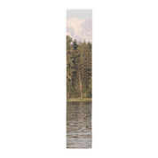 Tall pine trees reflected in water with snowy mountains above.