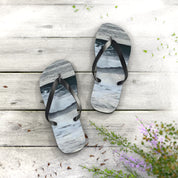 Flip-flops with ocean wave design on a wooden surface with green sprigs.