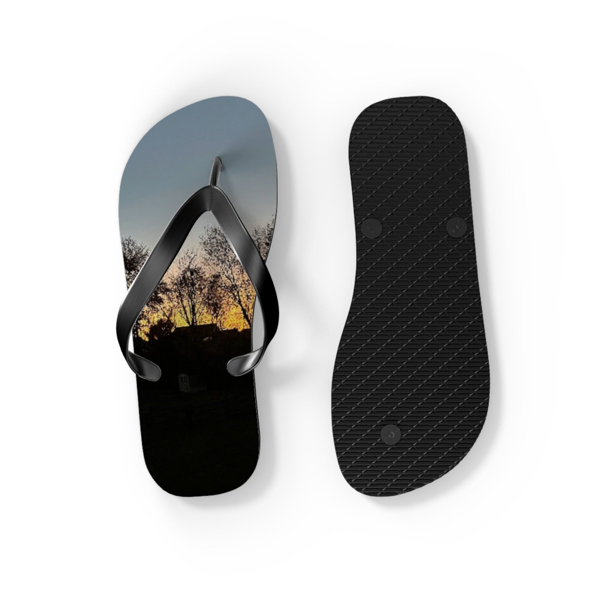 Black flip-flops with sunset landscape design on white background.