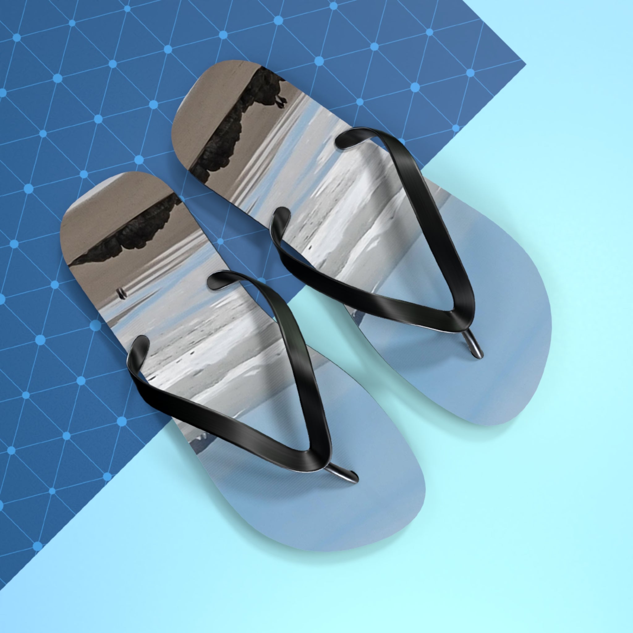 Flip-flops with abstract beach scene design and black straps on blue background.