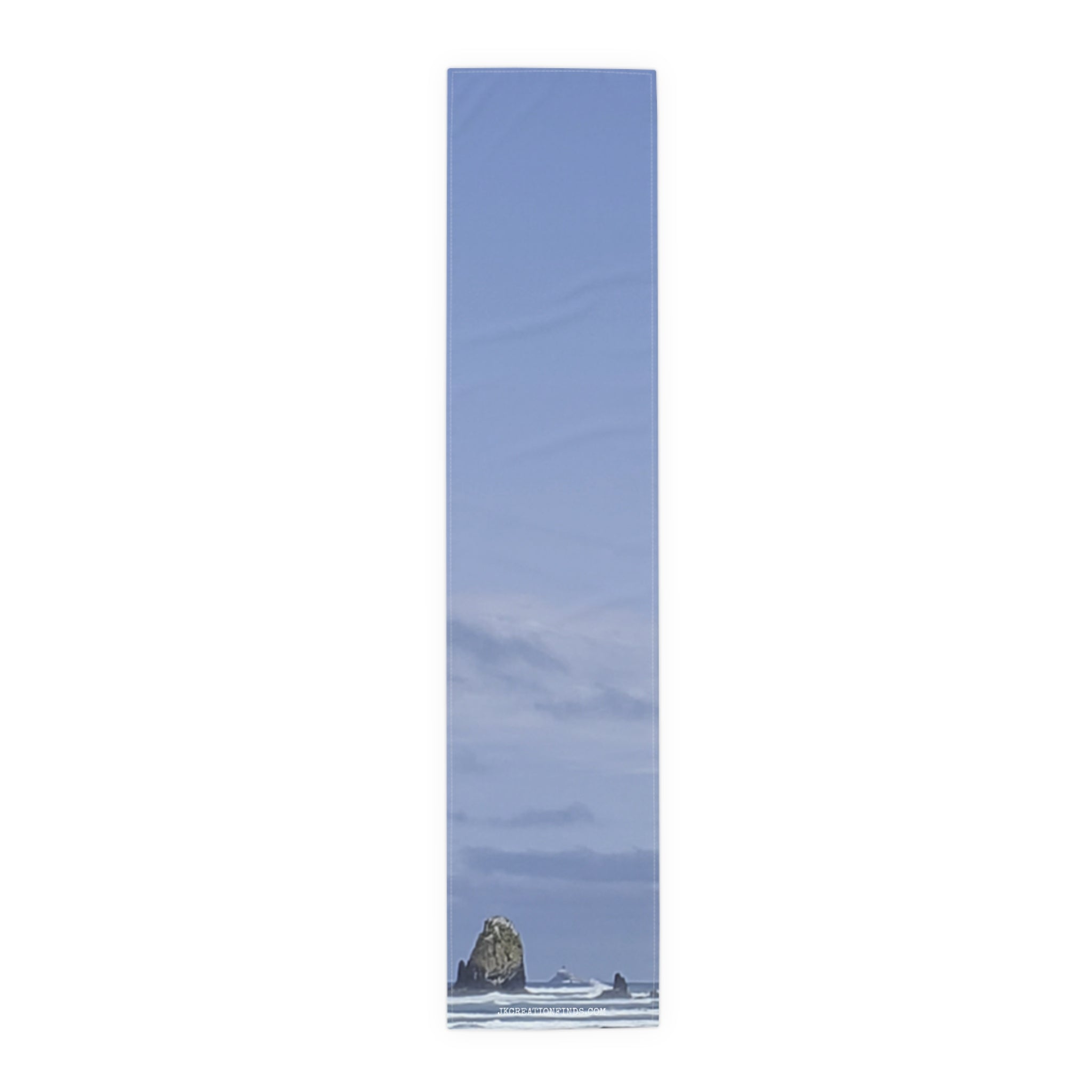 Tall, narrow image showing a rocky sea stack against a pale blue sky with clouds.