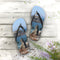 Flip-flops featuring a rocky ocean coastline scene, laid flat on wooden planks.