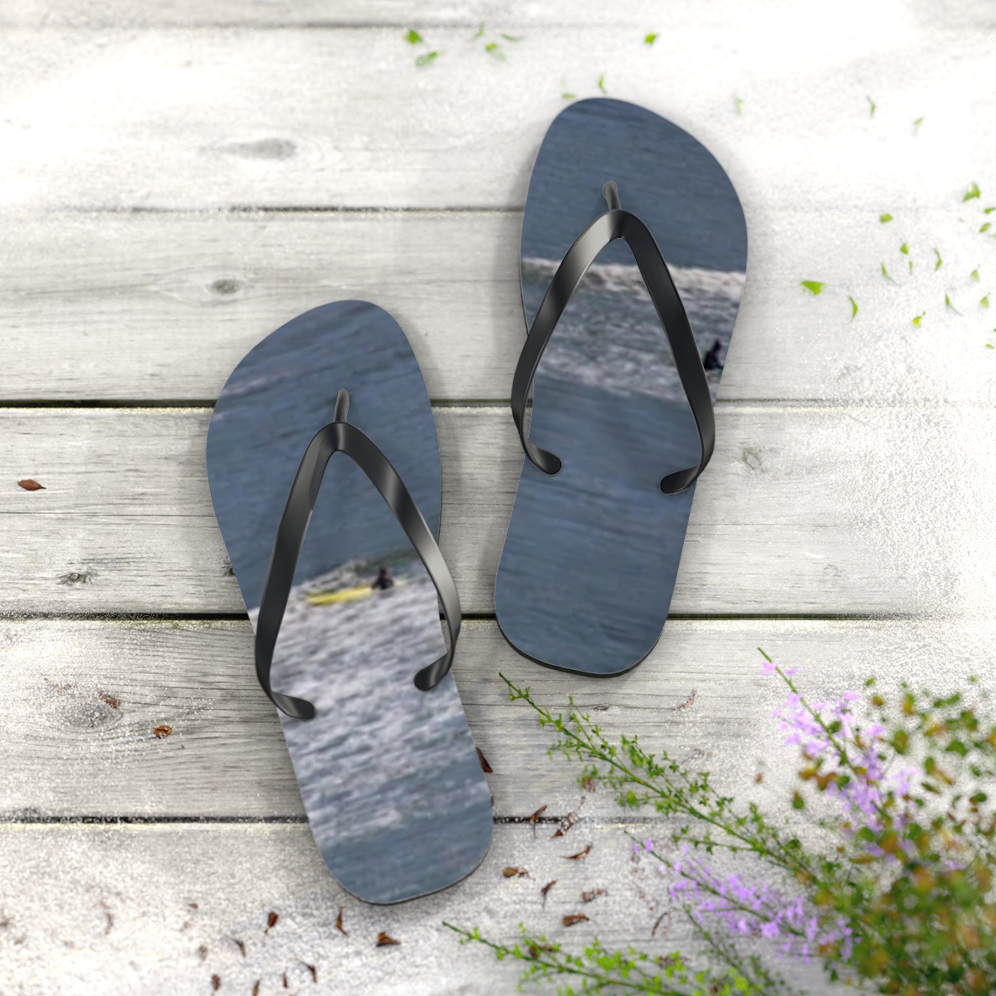 Flip-flops with ocean surf and surfers on a wooden deck.
