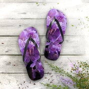 Purple floral flip-flops on a light wood background with green foliage.