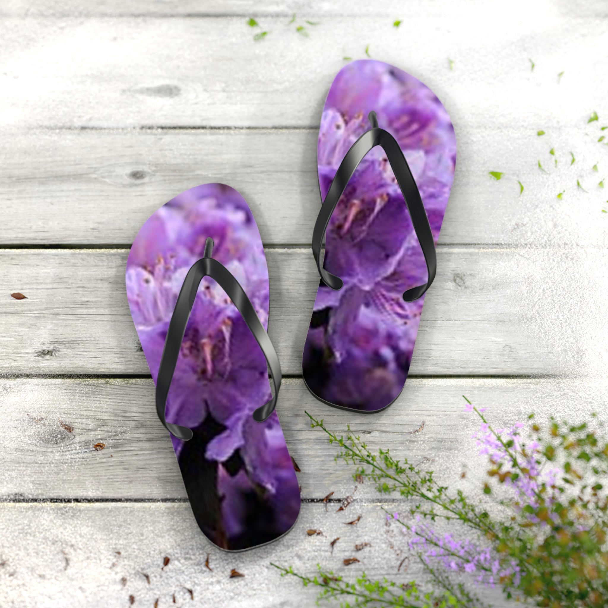 Purple floral flip-flops on a light wood background with green foliage.