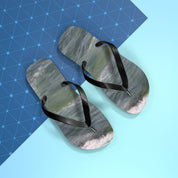 Black flip-flops with ocean wave pattern on blue and light blue background.