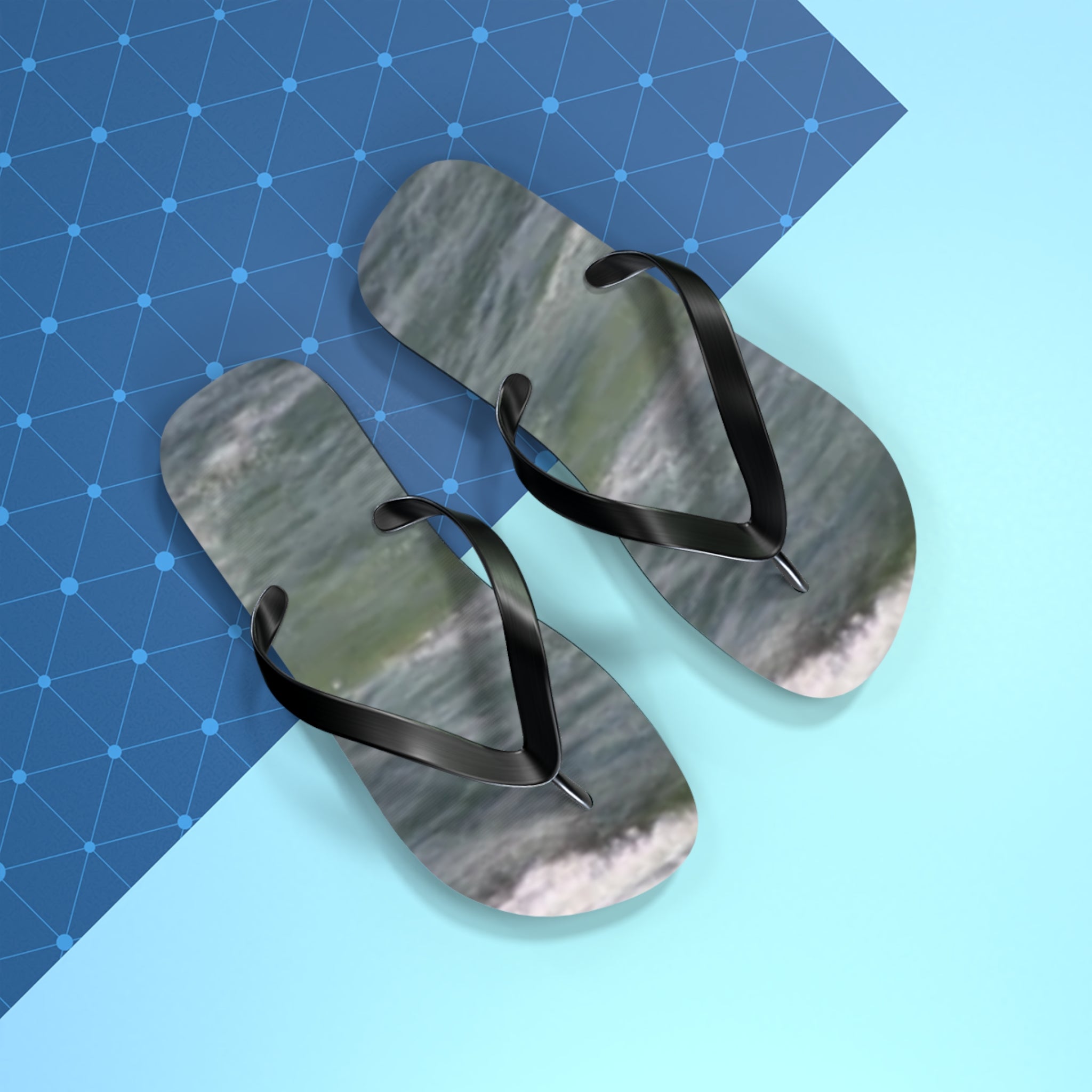 Black flip-flops with ocean wave pattern on blue and light blue background.