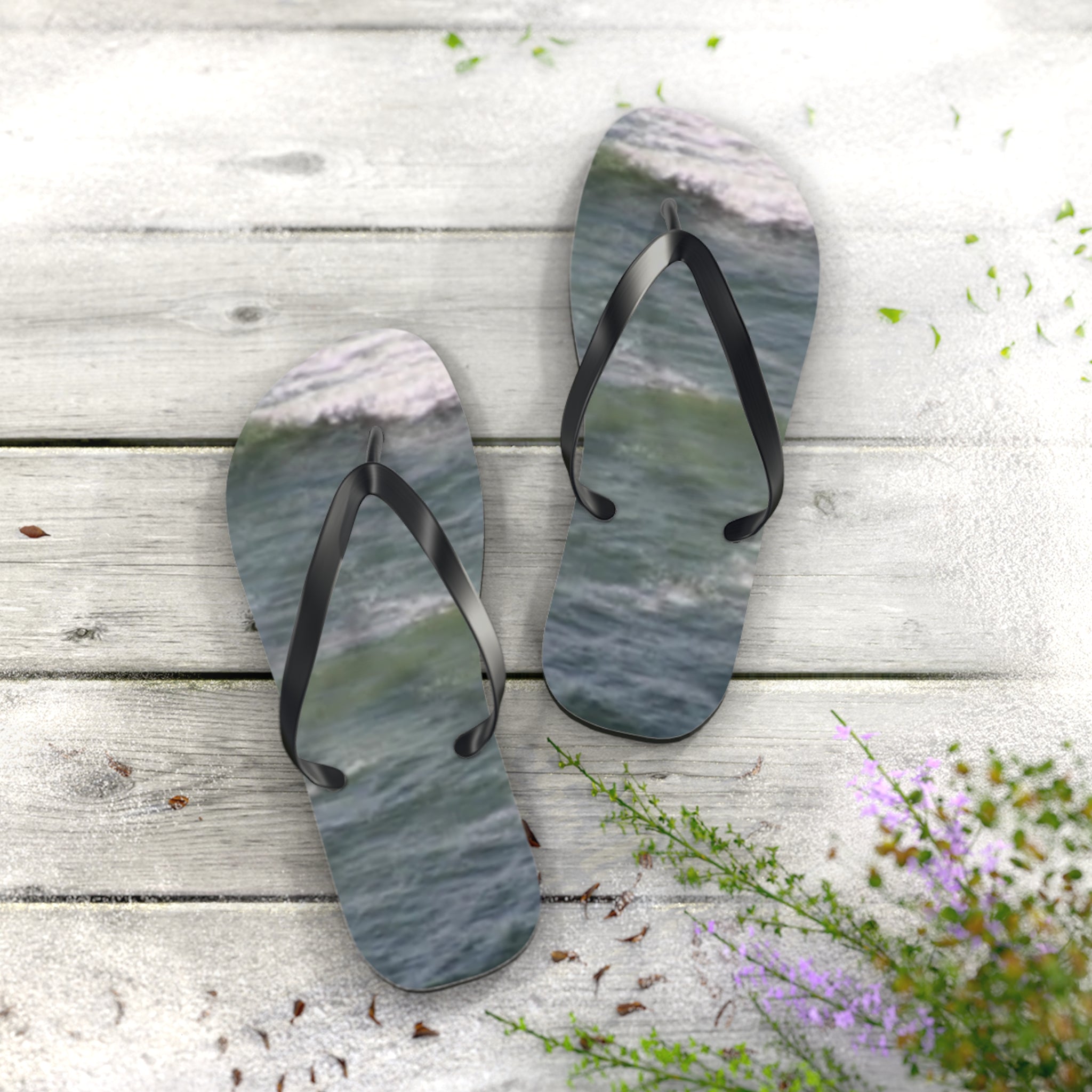 Flip-flops with ocean waves on a wooden deck with sand and flowers.