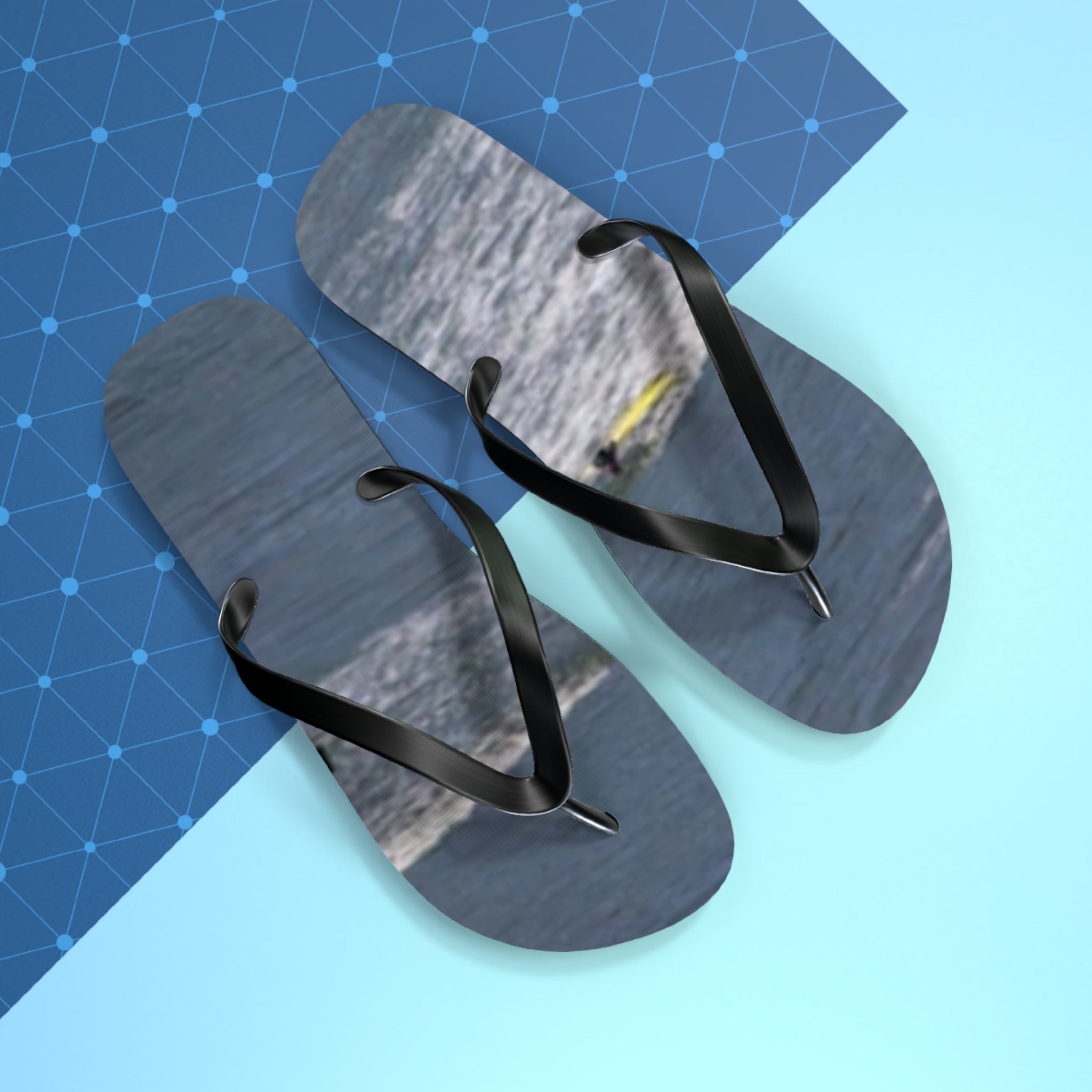Black flip-flops with a water scene on soles against a blue background.