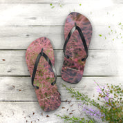 Pink floral flip-flops with black straps on weathered wooden planks.