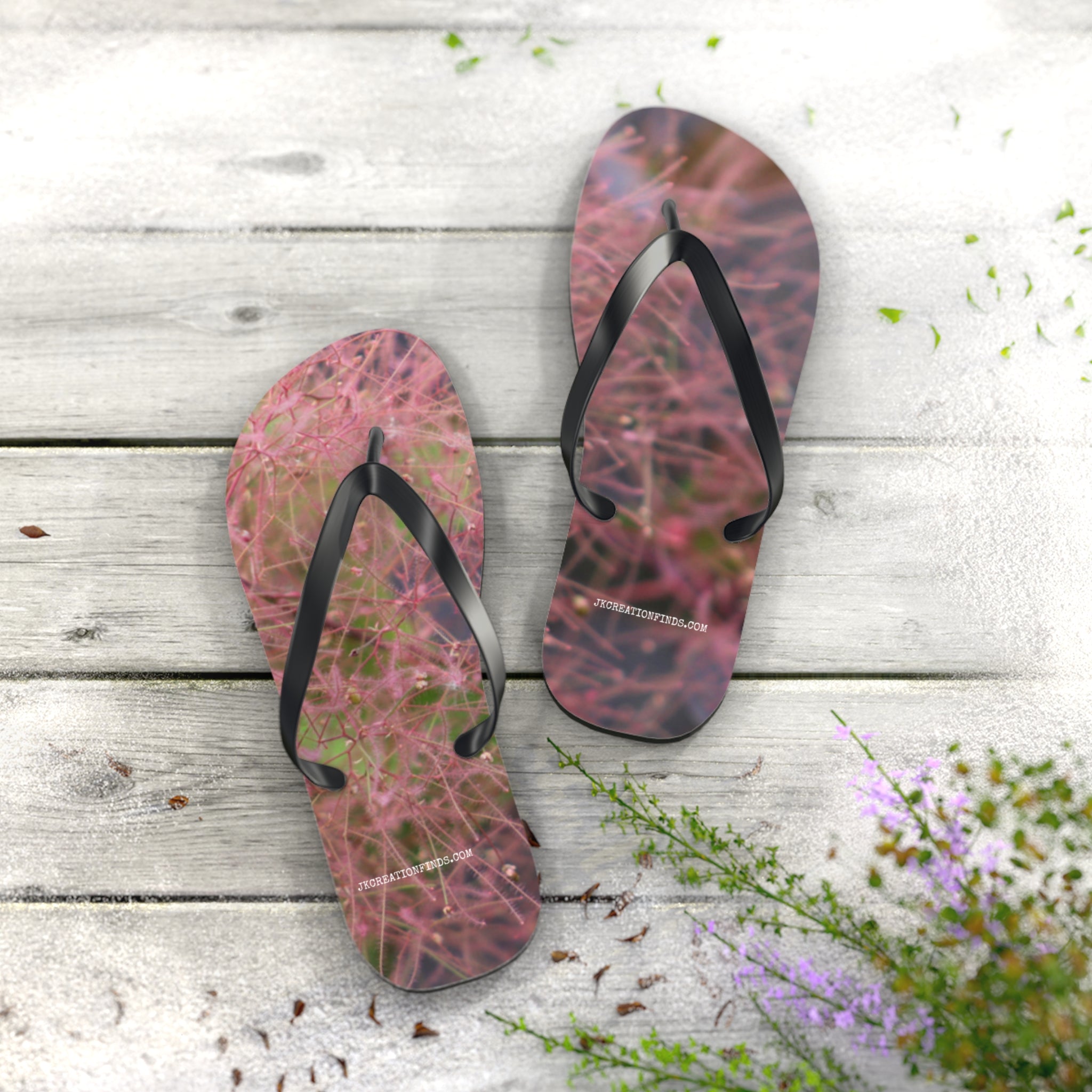 Pink floral flip-flops with black straps on weathered wooden planks.