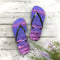 Purple flip-flops with a rocky shore design on a weathered wooden surface.