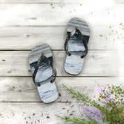 Flip-flops with a wave pattern on a wooden deck with scattered green leaves.