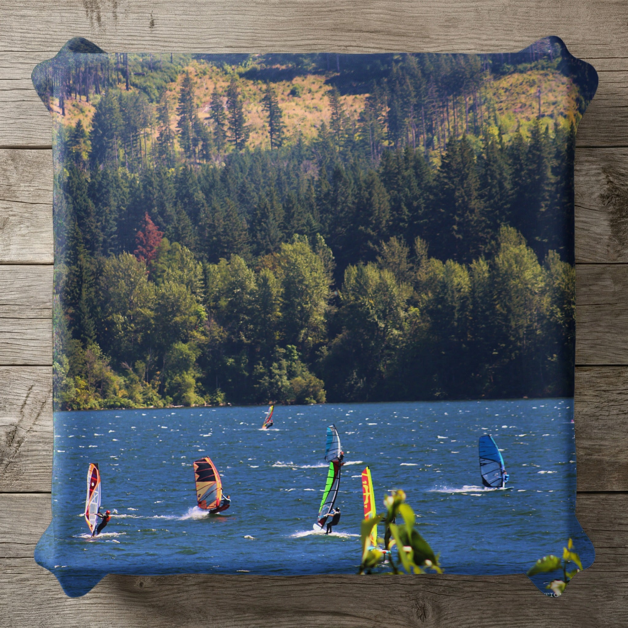 Windsurfers on a lake with a forested hillside in the background.