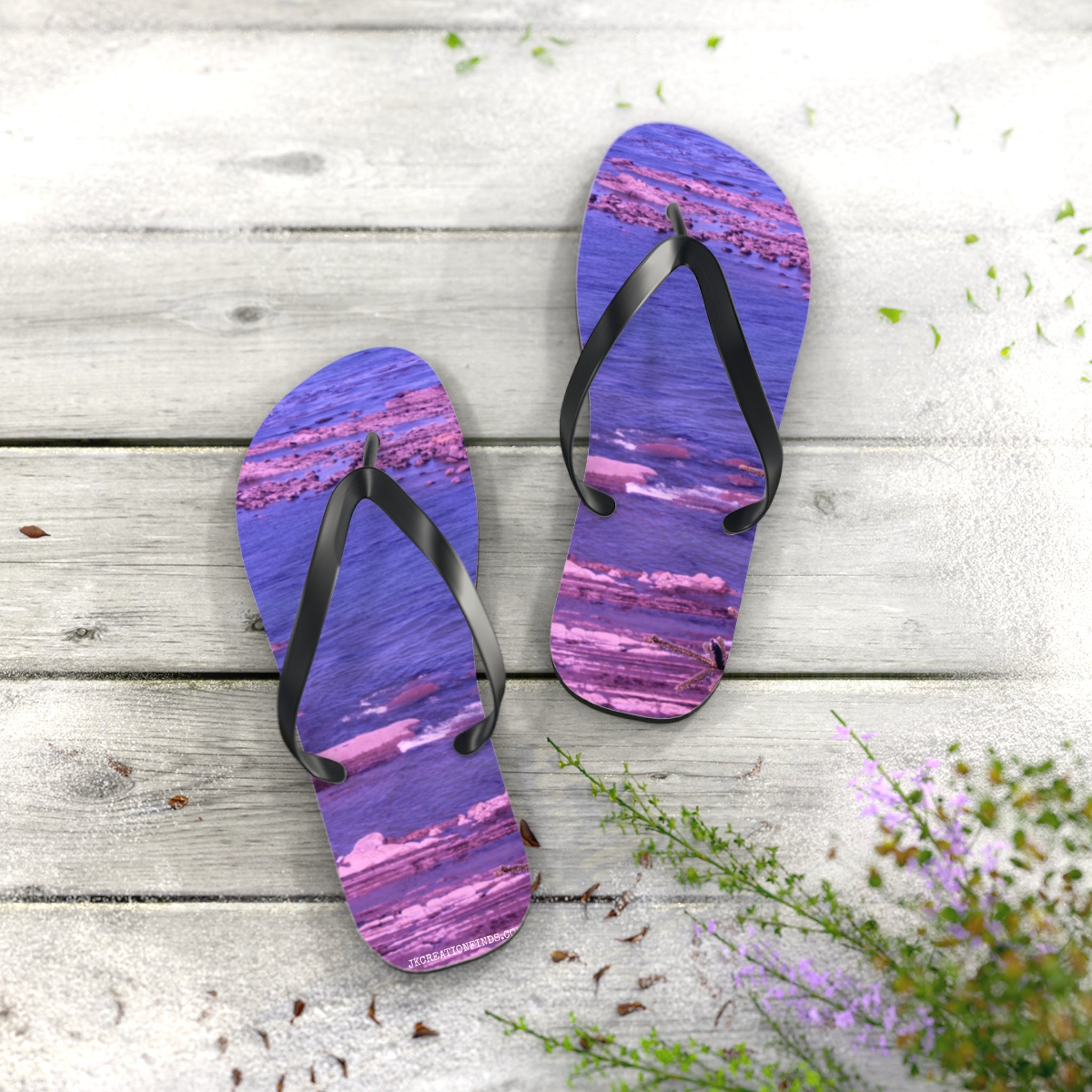 Purple and pink striped flip-flops on a wooden deck with scattered green leaves.