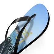 Black flip-flop with beach scene and gold logo on the sole.