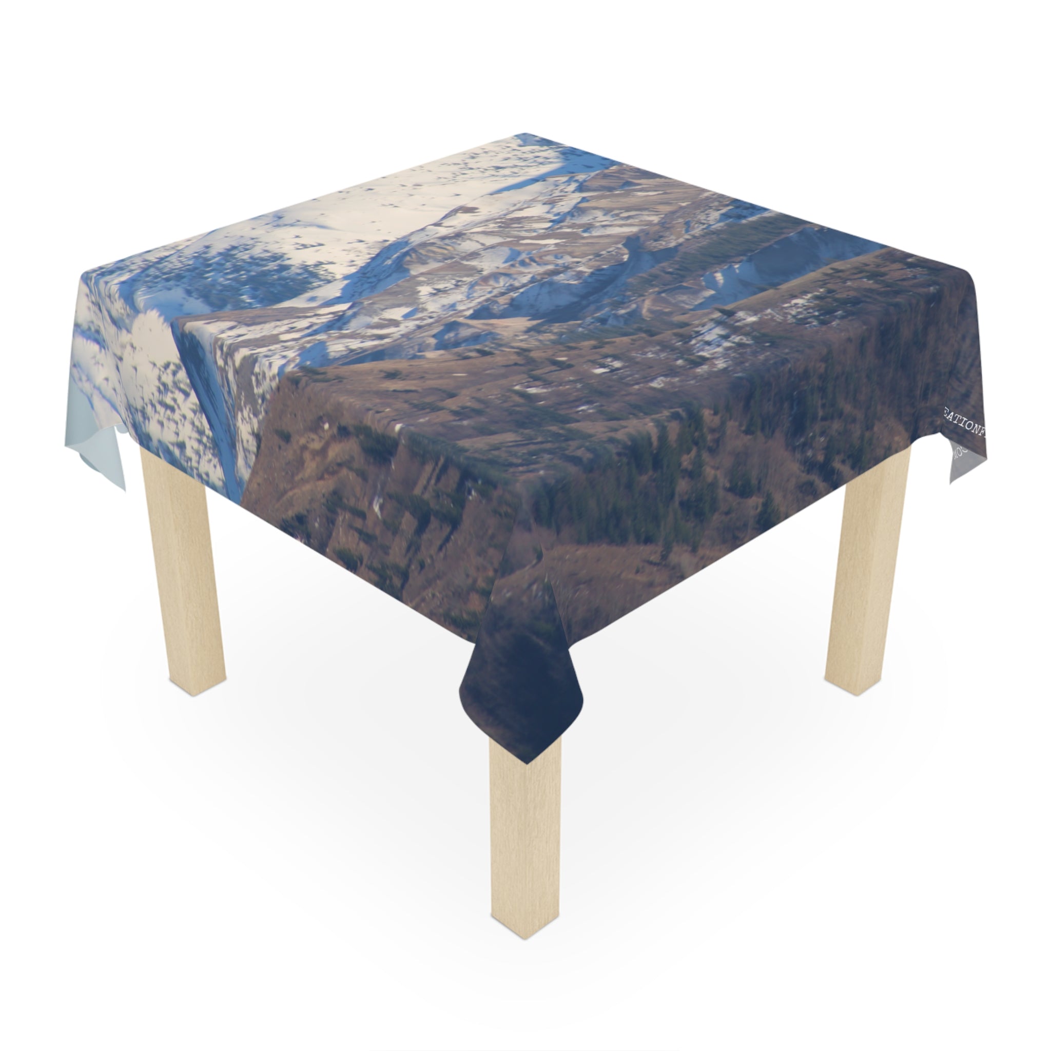 Tablecloth draped over a square table, featuring a mountainous landscape.