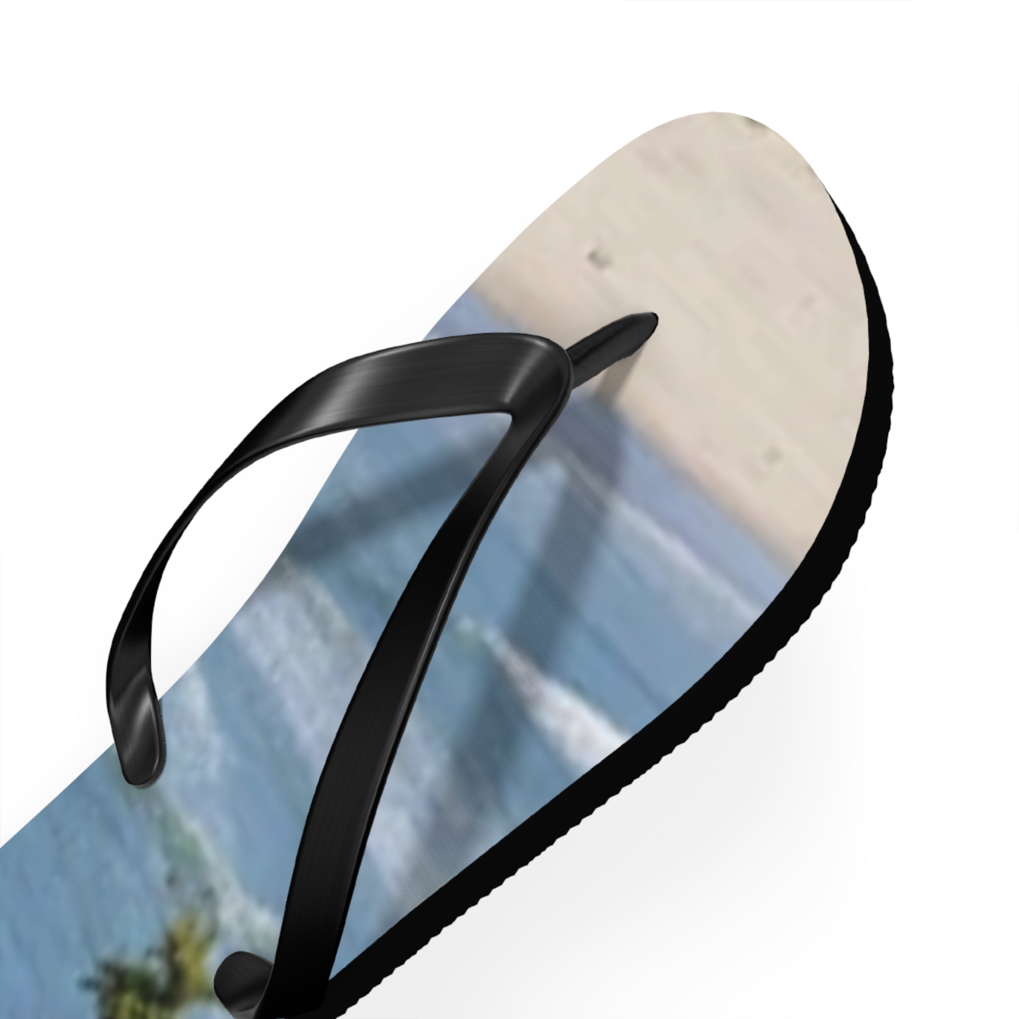 Black flip-flop with patterned sole depicting ocean waves and beach.
