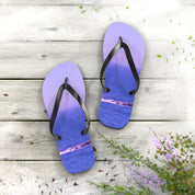 Purple flip-flops with ocean waves on wooden planks with flowers.