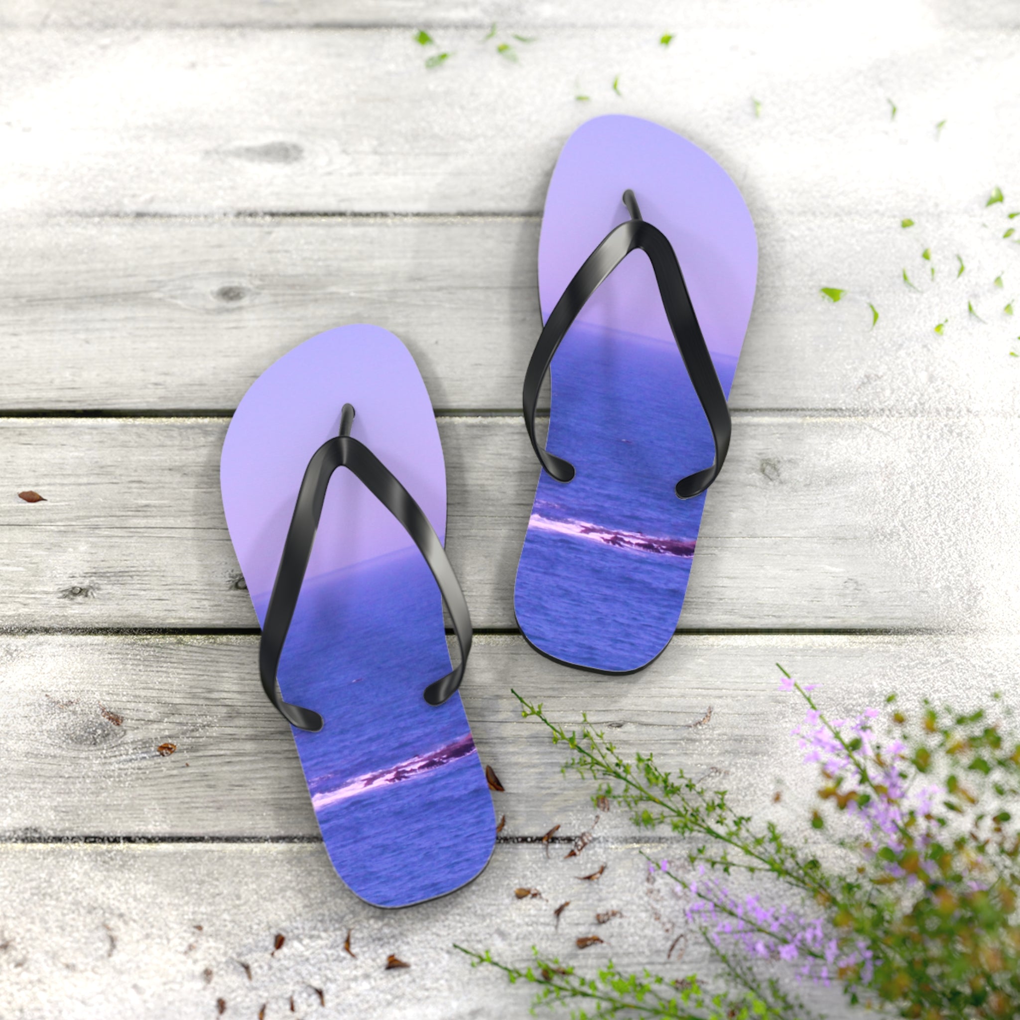 Purple flip-flops with ocean waves on wooden planks with flowers.