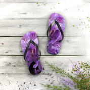 Purple floral flip-flops on a weathered wood surface with scattered petals.